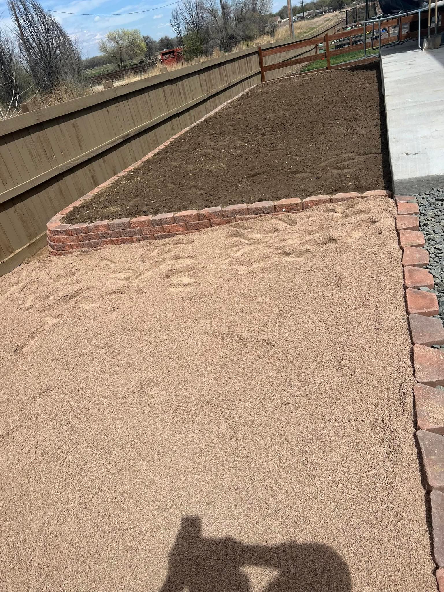 Landscape bed prepared with bare soil and brick edging along the grass line