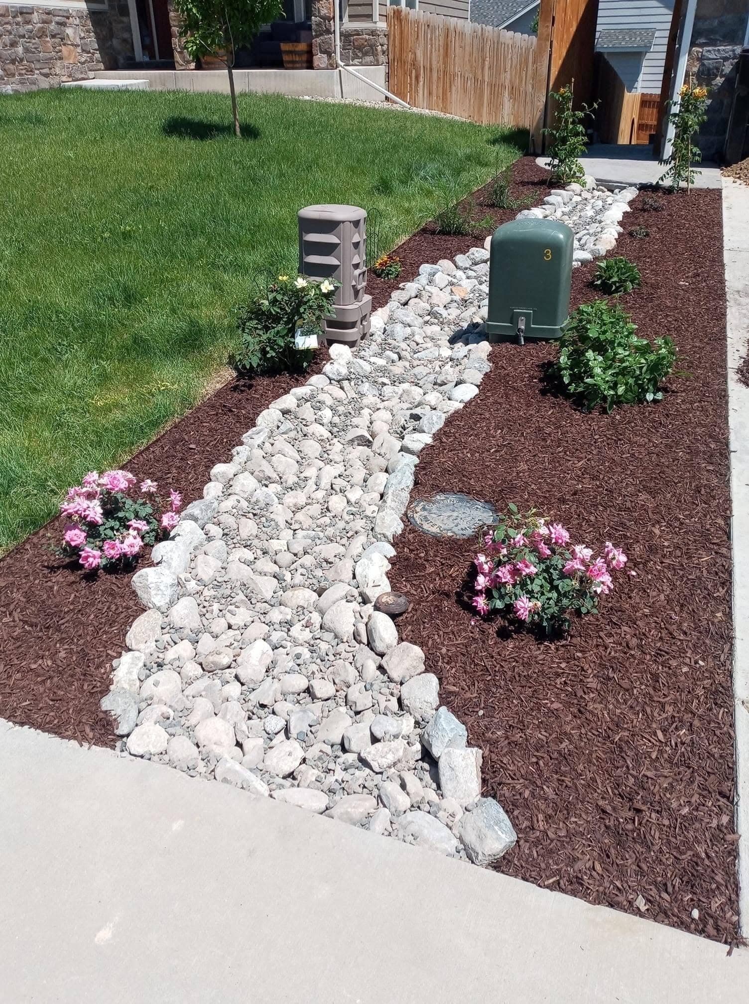 Completed landscape design with mulched bed, gravel pathway, and green sprinkler box