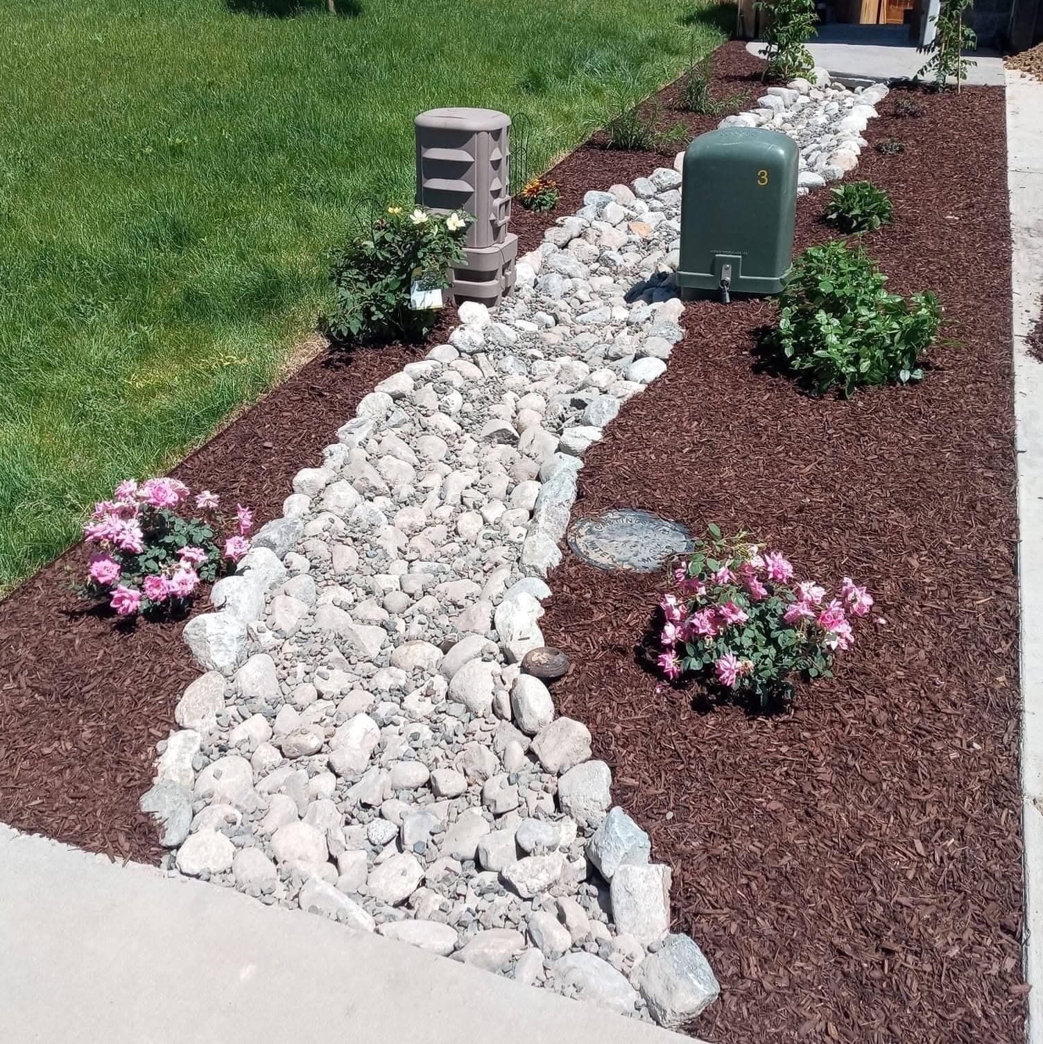 Finished landscape with white river-rock dry creek bed, dark mulch, and flowering plants